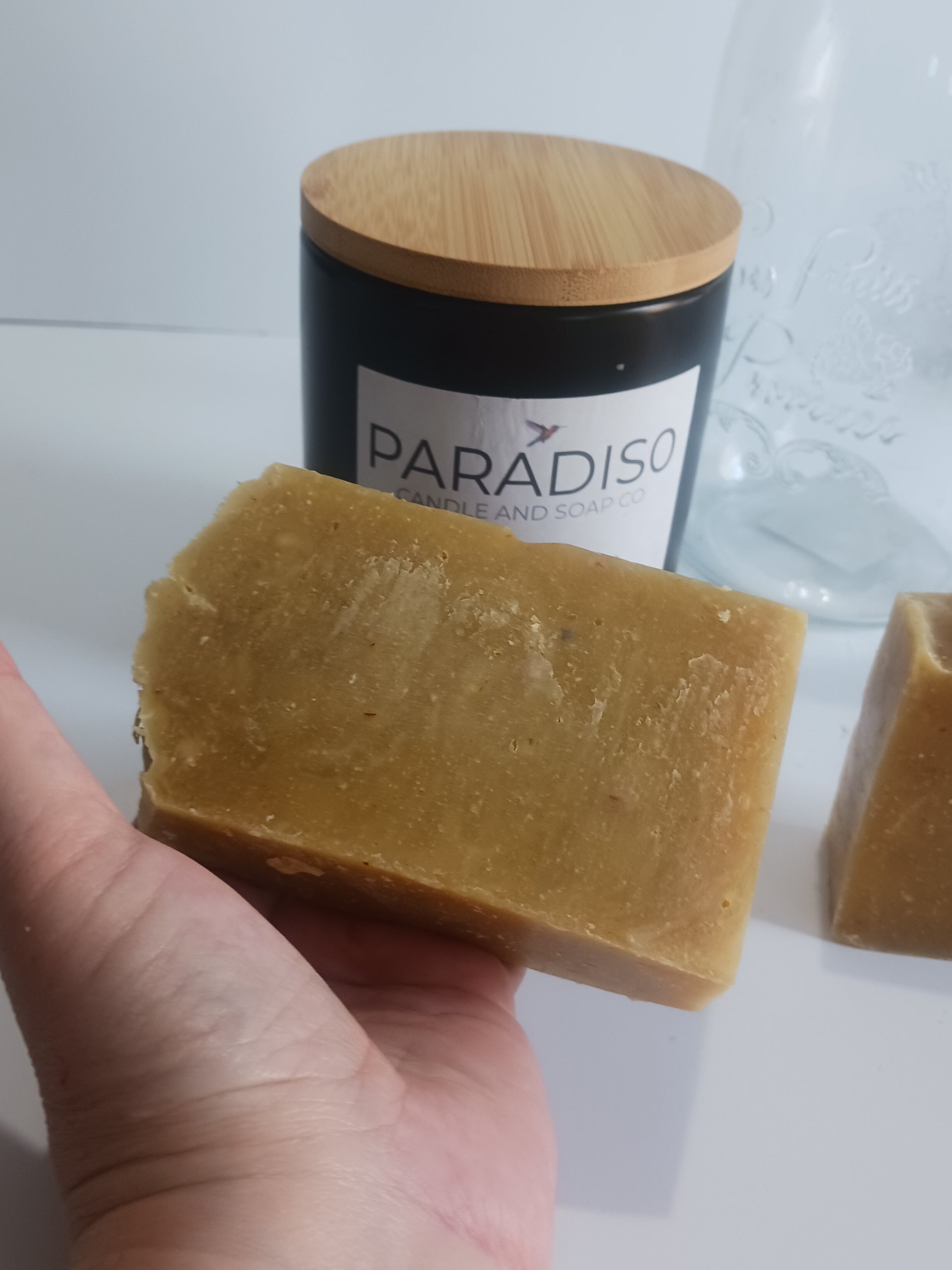Hand holding a bar of soap with matching  Papaia candle inackground