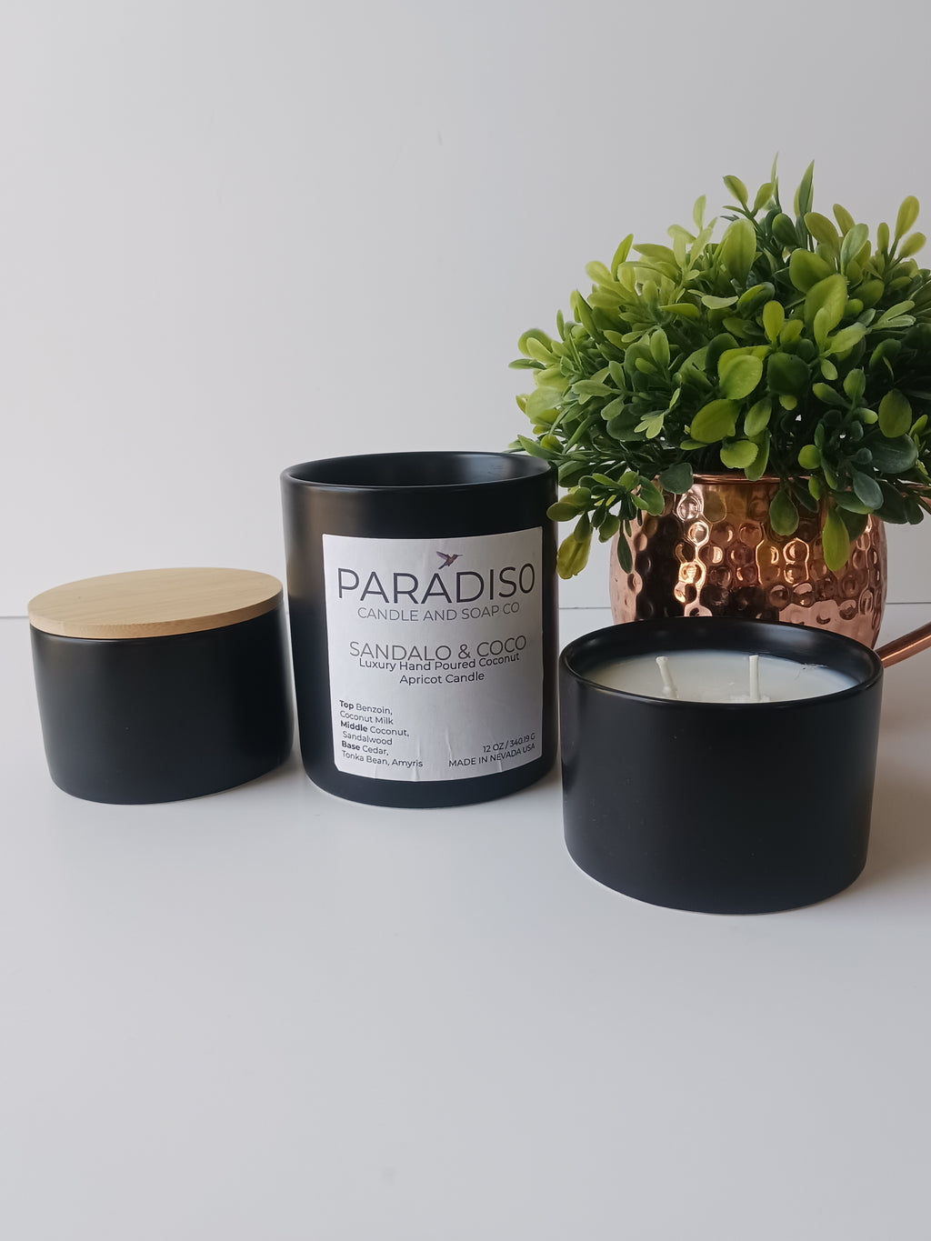 Black candle in a decorative container with a plant on a white surface